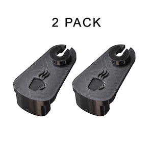 May include: Two black 3D-printed coffee cup holders. Each holder has a coffee cup design and a curved top. The text "2 PACK" is above the holders.