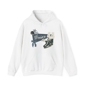 Op de afbeelding: Witte hoodie met een voorzak. Het ontwerp toont een hockeypuck, sterren en een banner met het woord "Briar" en het nummer "44". Een paar schaatsen is ook in het ontwerp opgenomen.