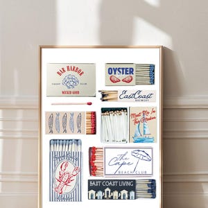 May include: A framed print featuring various matchbox designs with coastal themes. Designs include "Bar Harbor Yacht Club," "Oyster Bar," "East Coast Brewery," and "The Cape Beach Club." The color palette includes red, blue, and white.