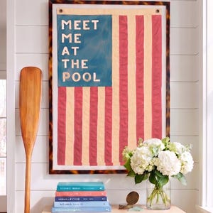 May include: A rectangular wall art piece featuring a flag design with alternating cream and red vertical stripes and a blue canton. The text "MEET ME AT THE POOL" is printed in white on the blue section. The piece is enclosed in a tortoiseshell frame.