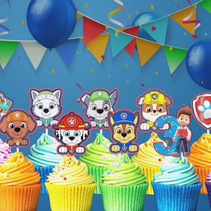 May include: A set of Paw Patrol themed cupcake toppers featuring various character faces, the Paw Patrol logo, a number three, and a lookout tower, displayed on colorful frosted cupcakes against a blue background with party bunting and balloons.