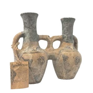 May include: Two-handled ceramic vase with a connecting bridge. The vase has a light brown base with gray and blue accents. The vase is decorated with floral and geometric patterns. A tag with the word "Ambiance" is attached.