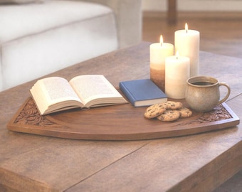 Può includere: Un vassoio di legno con dettagli floreali intagliati contiene un libro aperto, un piccolo libro blu, candele accese, una tazza di caffè e biscotti con gocce di cioccolato. Gli oggetti sono disposti su un tavolo di legno.