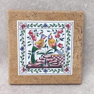 May include: A square cork coaster with a decorative ceramic tile insert. The tile features two colourful birds perched on a floral branch, surrounded by a border of flowers and leaves. The birds have blue, yellow, and green feathers.