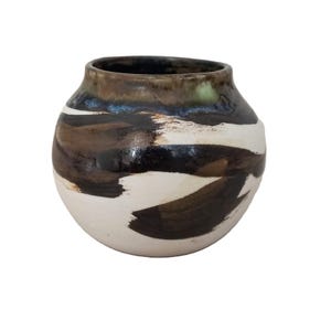 May include: A ceramic vase with a rounded body and a wide opening. The vase has a white base with brown and black brushstrokes. The rim is dark brown. This decorative vase is suitable for home decor.