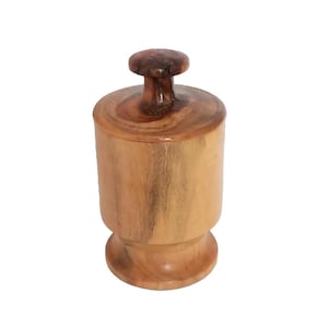 May include: A handcrafted wooden container with a lid. The container is cylindrical with a rounded base and a small, mushroom-shaped knob on top. The wood grain is visible, showcasing a mix of light and dark brown tones.