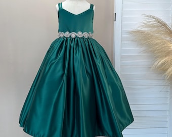Op de afbeelding: Een groene satijnen jurk met een V-hals lijfje en een volle rok. De jurk heeft een sierlijke riem in de taille en dunne bandjes. De jurk wordt op een mannequin gepresenteerd. Geschikt voor speciale gelegenheden.