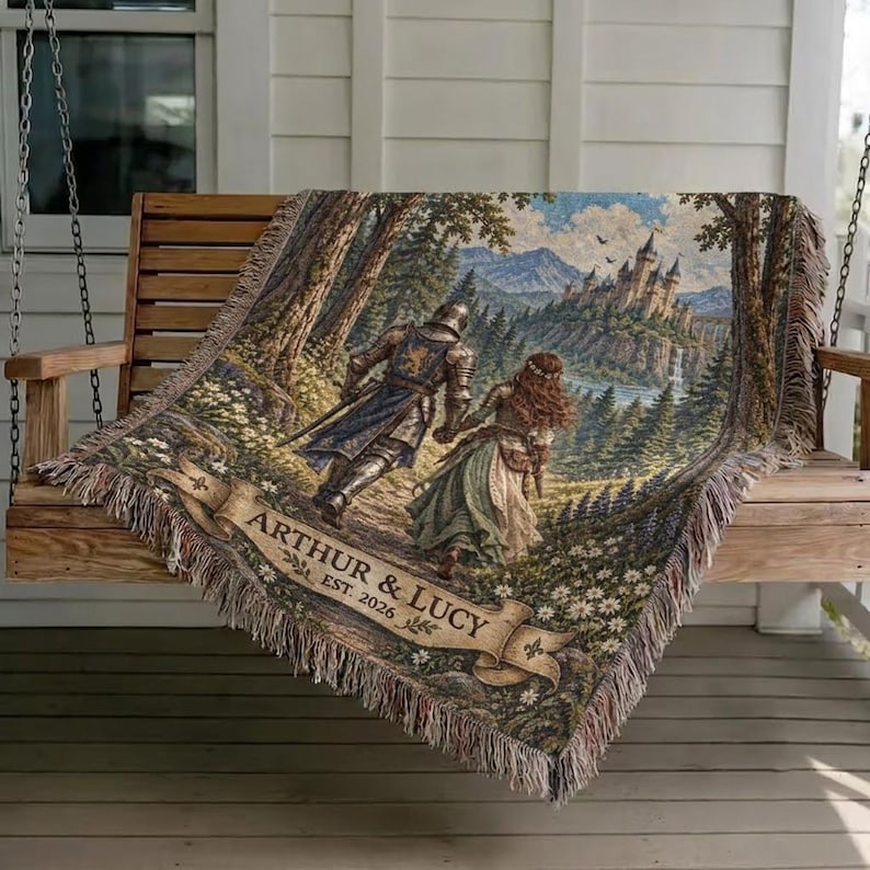Pu&ograve; includere: Una coperta tessuta con una scena fantasy raffigurante un cavaliere e una persona in abito che camminano attraverso un bosco verso un castello. Un cartiglio in basso riporta il testo ARTHUR & LUCY EST. 2026. La coperta ha bordi sfrangiati.