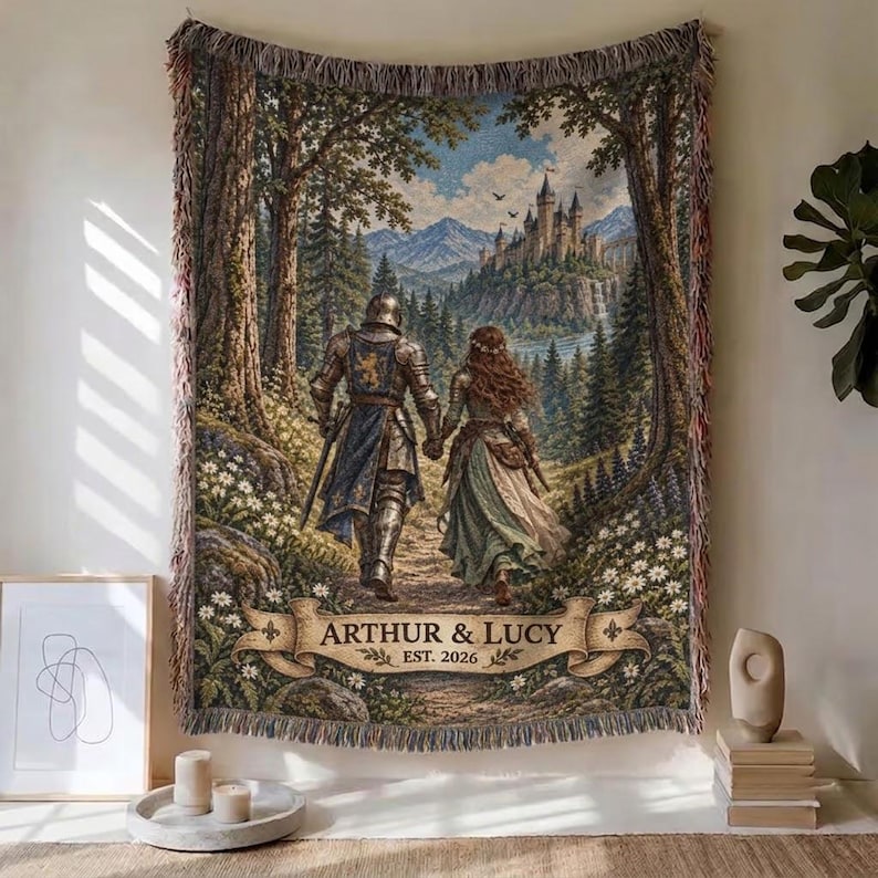 Pu&ograve; includere: Una coperta in arazzo intrecciato raffigurante un cavaliere in armatura e una persona con un abito lungo che camminano attraverso una foresta verso un castello. La scena include uno stendardo in basso con il testo ARTHUR & LUCY EST. 2026 e frange.