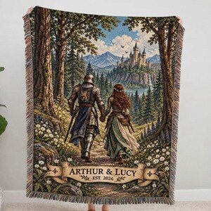 Pu&ograve; includere: Una coperta tessuta che raffigura un cavaliere in armatura e una persona con un abito lungo che camminano attraverso una foresta verso un castello. La scena include uno stendardo in basso con il testo ARTHUR & LUCY EST. 2026 e frange decorative.