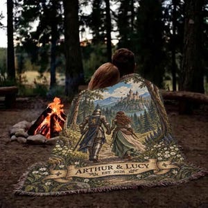 Pu&ograve; includere: Una coperta tessuta che raffigura una scena medievale con un cavaliere e una persona in abito che camminano verso un castello. Il design include un nastro con il testo ARTHUR & LUCY EST. 2026, circondato da un paesaggio boschivo con fiori.