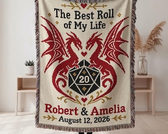 Può includere: Una coperta intrecciata color crema con due draghi rossi uno di fronte all'altro, che fiancheggiano un dado nero a venti facce con il numero 20. Il testo recita: The Best Roll of My Life, Robert & Amelia e August 12, 2026, con cuori rossi.