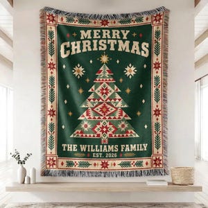Può includere: Una coperta tessuta con sfondo verde scuro caratterizzata da un motivo centrale geometrico ad albero di Natale, il testo MERRY CHRISTMAS, THE WILLIAMS FAMILY ed EST. 2026, incorniciata da un bordo decorativo con stelle rosse e rami di pino verdi.