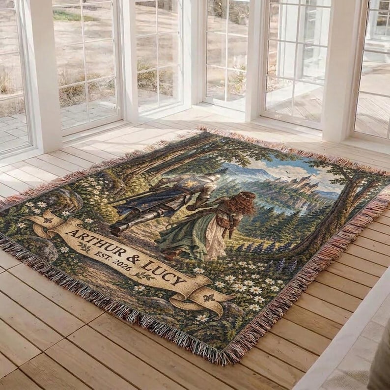 Pu&ograve; includere: Una coperta in arazzo intrecciato che raffigura una scena fantasy con un cavaliere e una persona in abito che camminano attraverso una foresta verso un castello lontano. Un banner beige in basso mostra il testo ARTHUR & LUCY EST. 2026 con frange.