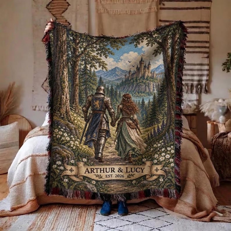 Pu&ograve; includere: Una coperta tessuta con una scena fantasy che ritrae un cavaliere in armatura e una persona con un abito lungo che camminano verso un castello in lontananza. Il testo ARTHUR & LUCY EST. 2026 &egrave; stampato su un banner in basso. La coperta ha frange.