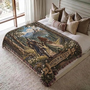 Pu&ograve; includere: Una coperta tessuta che raffigura una scena fantasy con un cavaliere e una persona dai capelli lunghi che camminano attraverso una foresta verso un castello. Un banner beige in basso mostra il testo ARTHUR & LUCY EST. 2026. La coperta ha frange.