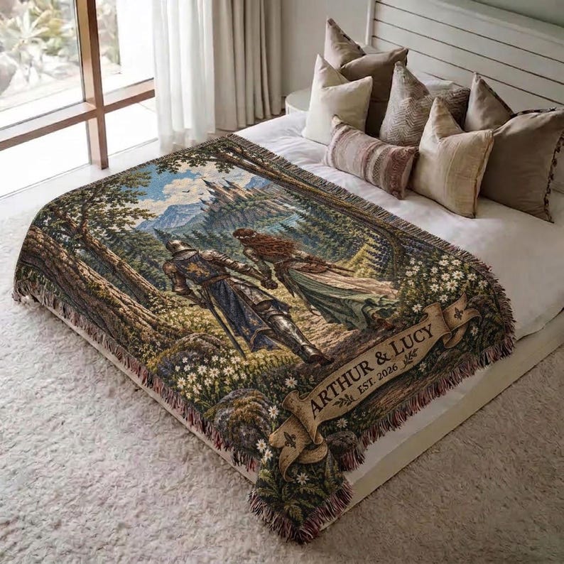 Pu&ograve; includere: Una coperta tessuta che raffigura una scena fantasy con un cavaliere e una persona dai capelli lunghi che camminano attraverso una foresta verso un castello. Un banner beige in basso mostra il testo ARTHUR & LUCY EST. 2026. La coperta ha frange.