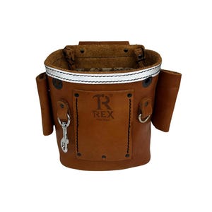 May include: A brown leather tool bag with the text "R REX Test Bags" on the front. The bag has a silver-colored clip and a white reflective stripe around the top. Two smaller pockets are on the sides.