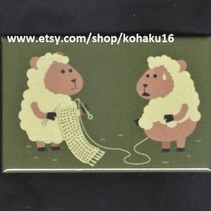 May include: A rectangular magnet featuring two cartoon sheep on a green background. One sheep knits a scarf, while the other looks on with a worried expression. The text "www.etsy.com/shop/kohaku16" is at the top.