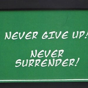 May include: Green motivational sign with white text that reads "Never give up! Never surrender!"