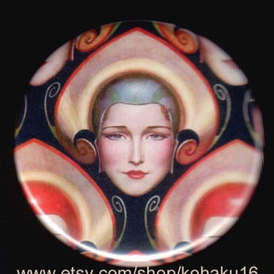 May include: A vintage-style button featuring a woman's face in a geometric design. The woman has light skin, dark hair, and is wearing a light blue hat. The background is a dark blue with a repeating pattern of swirls and lines.