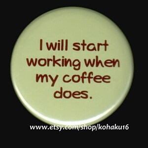 May include: A round, light green button with the text "I will start working when my coffee does." in brown lettering. The text is centered on the button. The button has a white border and a website address printed on the bottom: www.etsy.com/shop/kohaku16.