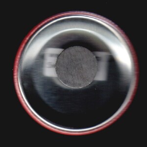 May include: Close-up of the back of a round button with a red border. The button has a silver surface with a black circle in the center.