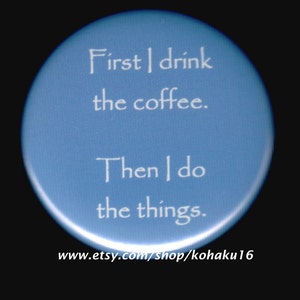 May include: A blue round button with white text that reads "First I drink the coffee. Then I do the things." The bottom of the button has the website address "www.etsy.com/shop/kohaku16".