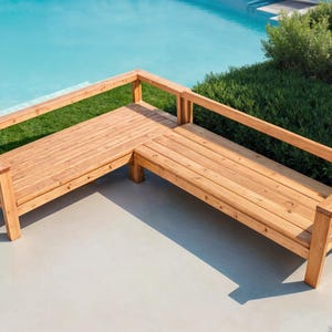 May include: A wooden L-shaped outdoor bench with a natural finish. The bench has a slatted seat and back, with a railing on the sides. The bench is made of light brown wood and is set on a concrete patio next to a pool and green grass.