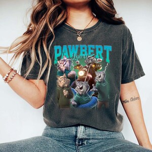 May include: Dark gray t-shirt featuring a graphic of cartoon cats with the text "PAWBERT Lynx". The cats are depicted in various poses, some wearing sweaters and riding a motorcycle. The design has a vintage, distressed look.