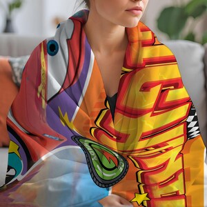 May include: A colorful blanket featuring a cartoon car design with the word "READY" and a checkered flag pattern. The blanket has a vibrant mix of red, orange, yellow, and blue hues, creating a dynamic and playful aesthetic.