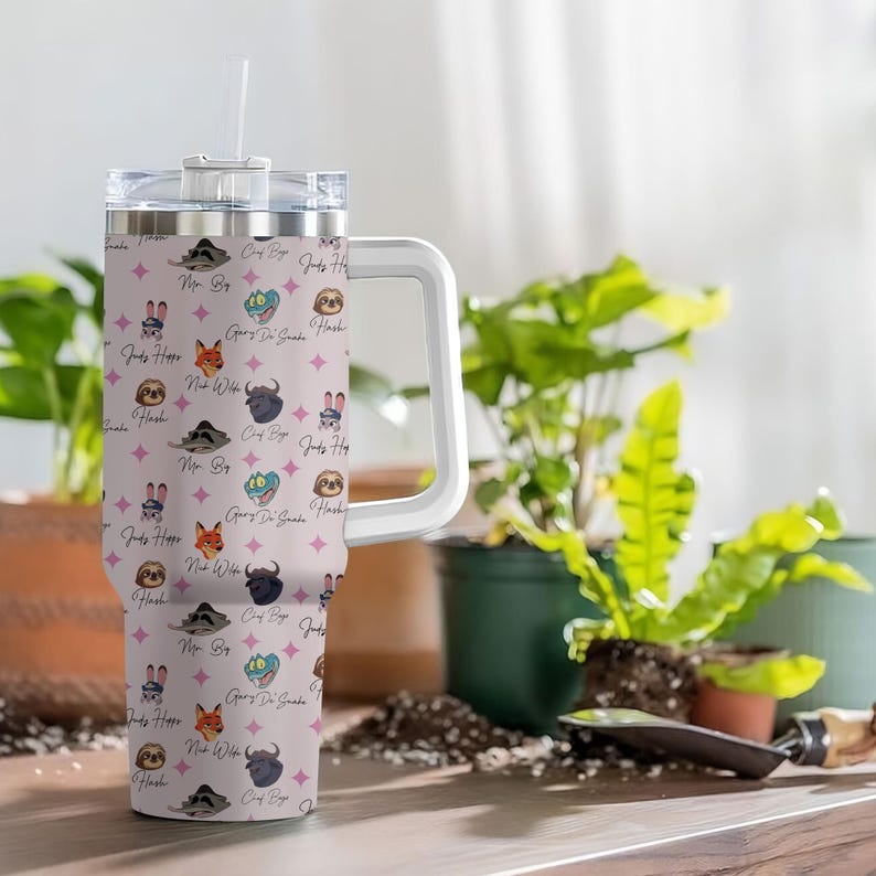 Puede incluir: Un vaso grande y aislado con asa y pajita blancas. El vaso presenta un fondo rosa claro con dise&ntilde;os repetidos de animales de dibujos animados y texto. Los animales incluyen un perezoso, un zorro y un conejo. El texto incluye frases como "Judy Hope" y "Gary Di Guate Hash."