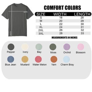May include: A dark grey t-shirt with size and colour options. The text "COMFORT COLORS" is at the top, with a size chart showing width and length measurements in inches. Colour swatches include Pepper, Ivory, and Blue Jean.
