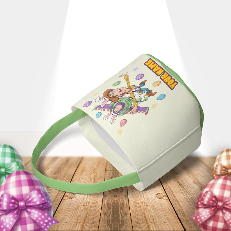 Puede incluir: Una cesta de Pascua de color crema con asa y ribete verdes. La cesta presenta una imagen de dibujos animados de Woody y Buzz Lightyear de Toy Story, con el texto "YOUR NAME". Huevos de Pascua decorativos est&aacute;n dispersos alrededor de los personajes.