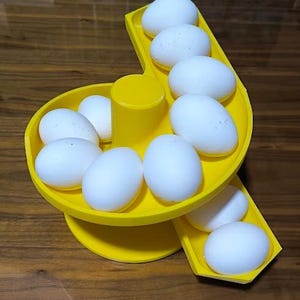 May include: A yellow plastic egg dispenser filled with white eggs. The dispenser has a tiered design with a central cylinder and angled tracks for the eggs to roll down. The eggs are arranged in a visually appealing manner.