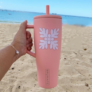 May include: A pink stainless steel travel mug with a white floral design and a handle. The mug has a straw and the text "BRÜMATE" is printed on the side.