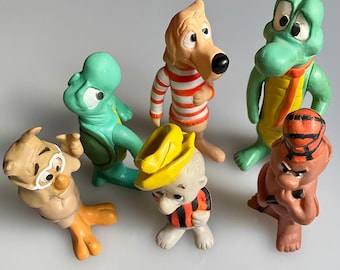 May include: A set of five vintage cartoon character figurines. The figurines are made of plastic and feature a turtle, a dog, a crocodile, a bird, and a boy wearing a hat. The figurines are painted in bright colors, including green, red, yellow, and brown.