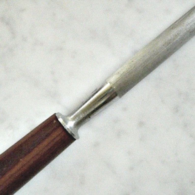 以下が含まれることがあります： 木製のハンドルが付いた銀色の金属製の包丁研ぎ器。ハンドルは濃い茶色で、滑らかな仕上がりです。