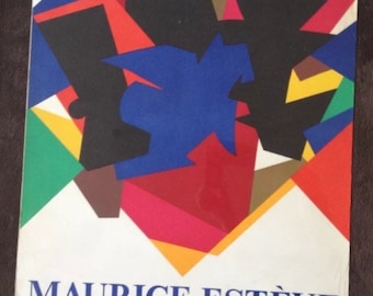 May include: A colorful abstract art poster advertising an exhibition of collages by Maurice Estève. The poster features a geometric design in red, blue, yellow, green, black, and brown. The text on the poster reads "Maurice Estève 1956 Collages 1973 23 Avril - 15 Juin 1974 Galerie Claude Bernard 5 & 7, Rue des Beaux-Arts Paris VI."