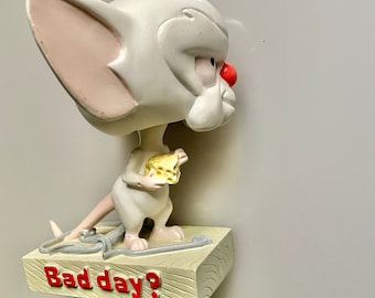 May include: A white cartoon mouse figurine holding a piece of cheese, standing on a wooden base with the text "Bad day?" in red letters.