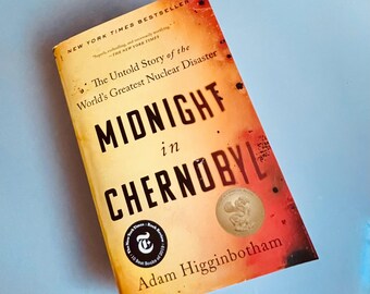 May include: A hardcover book titled "Midnight in Chernobyl" by Adam Higginbotham. The cover is a gradient of yellow and orange with black text. The book has a New York Times Bestseller banner and a "10 Best Books of 2019" sticker.