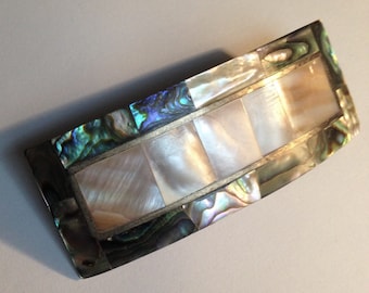 May include: A silver and iridescent abalone shell hair clip with a rectangular design. The clip has a curved shape and is made of multiple pieces of abalone shell.