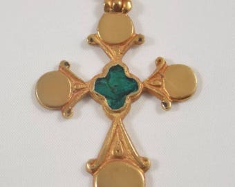 May include: Gold-toned cross pendant with a green center and circular accents. The cross is suspended from a gold chain. The design features a four-leaf clover shape in the center.
