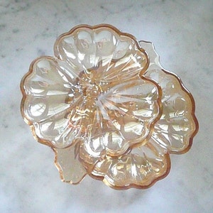 May include: A two-tiered iridescent glass candy dish shaped like a flower. The dish is made of clear glass with a pink and gold iridescent finish.