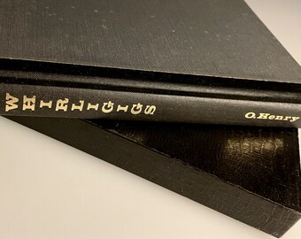May include: Two black hardcover books stacked on top of each other. The top book has the title "The Writings of O. Henry" in gold lettering.