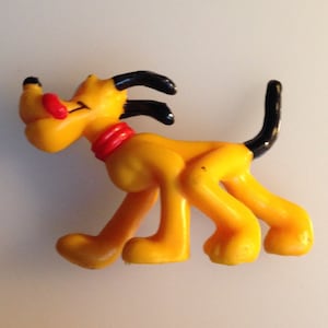 Könnte beinhalten: Gelber Plastik-Spielzeug-Hund mit schwarzen Ohren und Schwanz. Der Hund hat ein rotes Halsband und eine rote Nase.