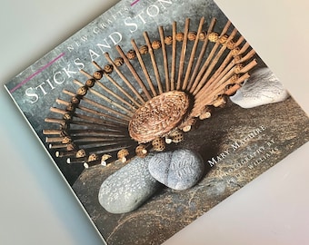 May include: Book cover with the title "Sticks and Stones: New Crafts" by Mary Maguire. The cover features a woven basket made of sticks and stones, with a brown background.