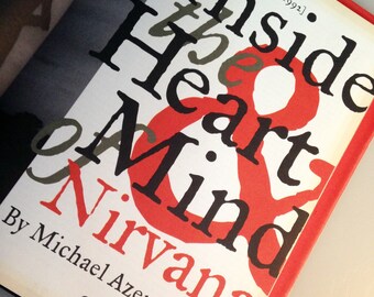 May include: A white book with red and black text that reads "Inside the Heart & Mind of Nirvana" by Michael Azerrad. The book cover also includes the date "April 16th, 1992" and the number "33".