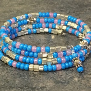 May include: A multi-strand bracelet with blue, pink, and silver beads. The bracelet is made of small, round beads and larger, square beads. The bracelet is wrapped around a wrist.