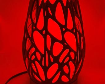 May include: A decorative lamp with a dark, patterned exterior and a bright red interior. The lamp's design features an intricate, openwork pattern that allows the red light to shine through. The lamp is plugged in and appears to be turned on.